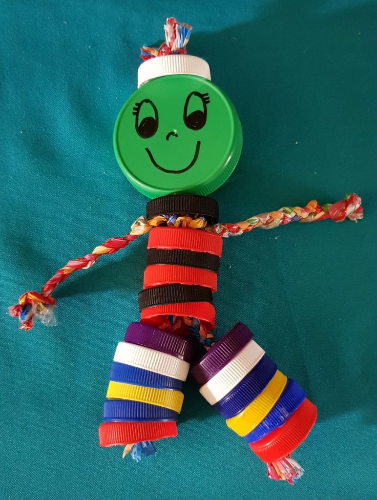 A picture of a handmade stick man made out of bottle caps and plastic bags.